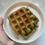 A hand holding a plate of crispy waffles that are tinted green