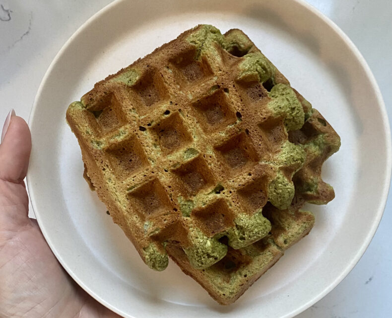 A hand holding a plate of crispy waffles that are tinted green