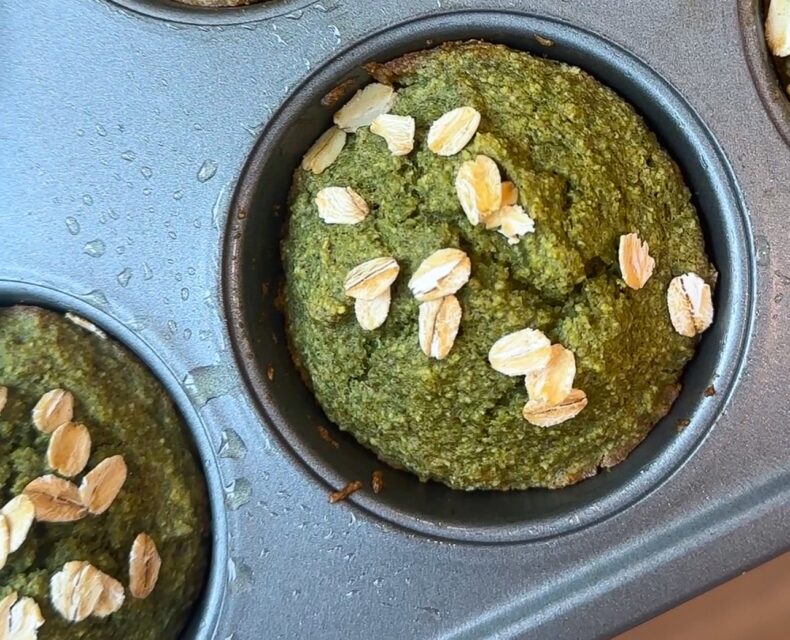 A picture of a muffin pan with green kale oat muffins with whole oats sprinkled on top