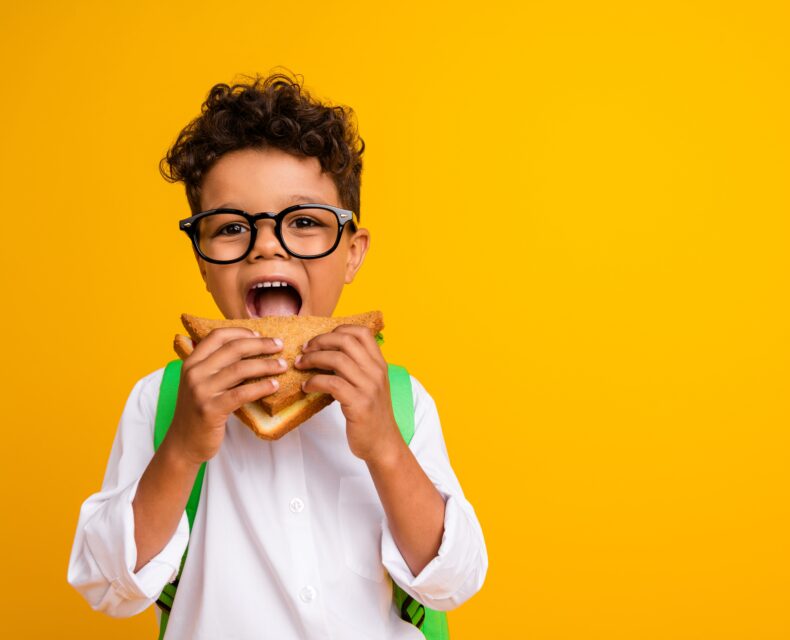 child taking a bite of a sandwich with an orange background