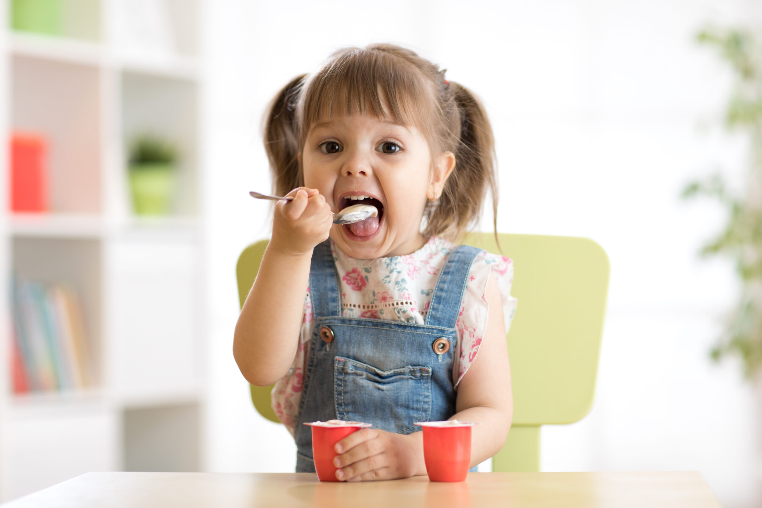 little girl with pigtails eating yogurt at the table