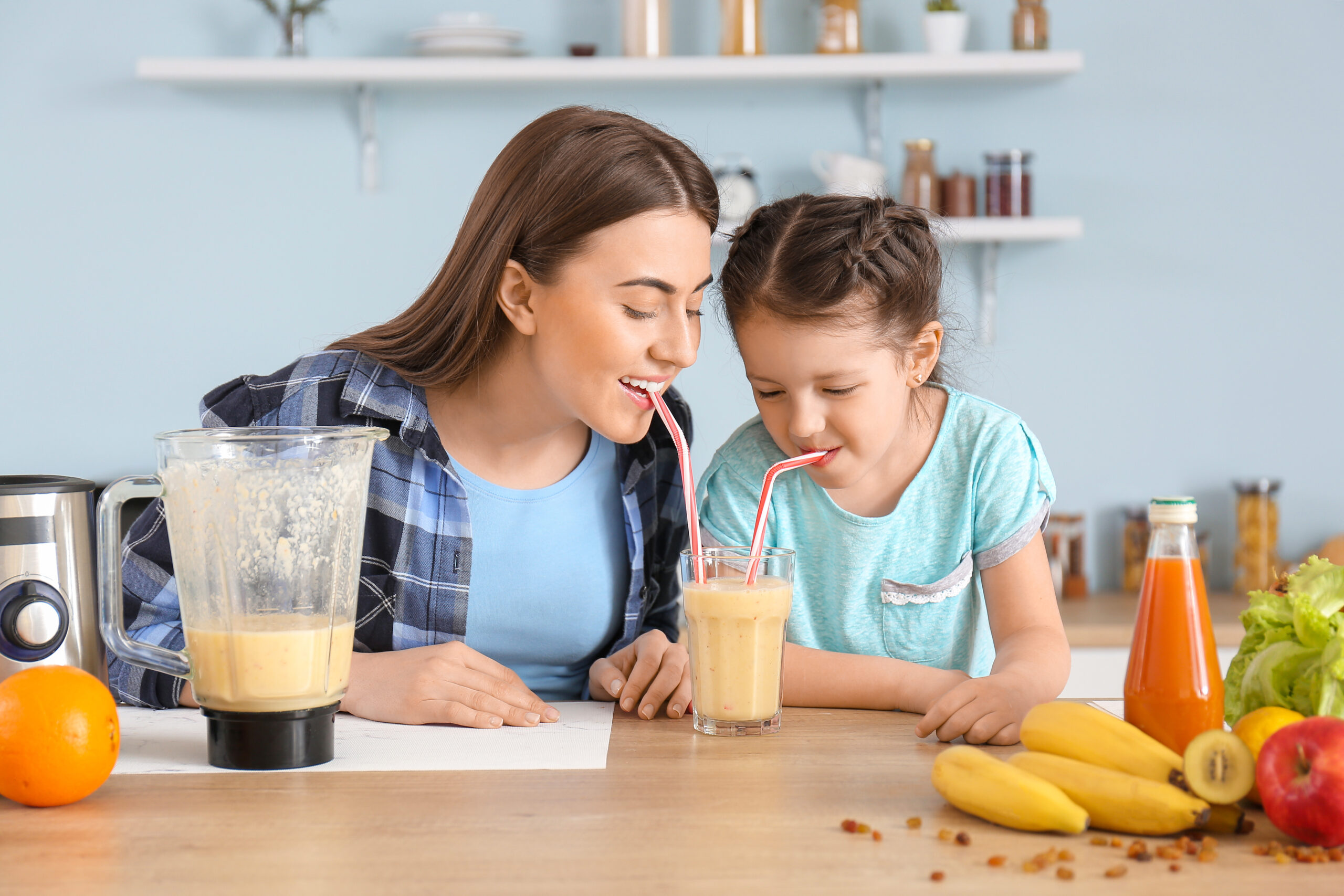 mom and daughter sharing two straws in an orange fruit smoothie at the table